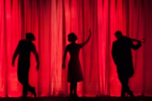 Silhouettes of 3 people in front of a red curtain. 