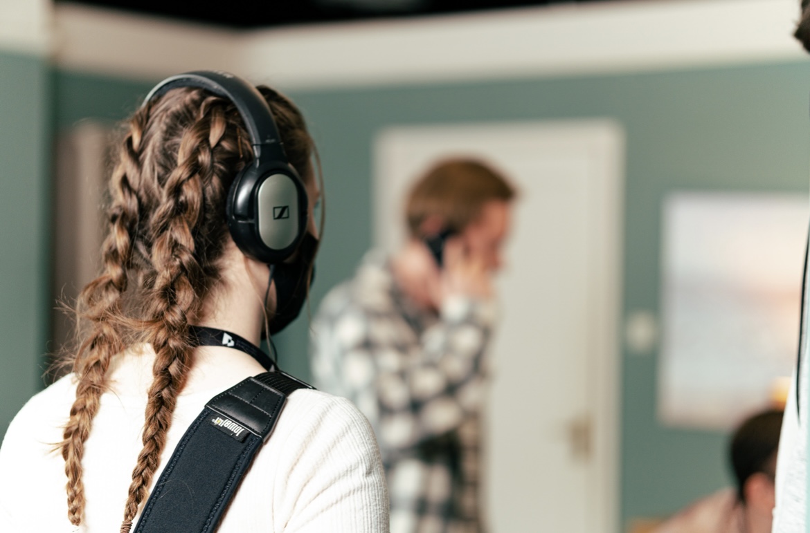 Young woman with plaits and over-ear headphones stands with back to camera