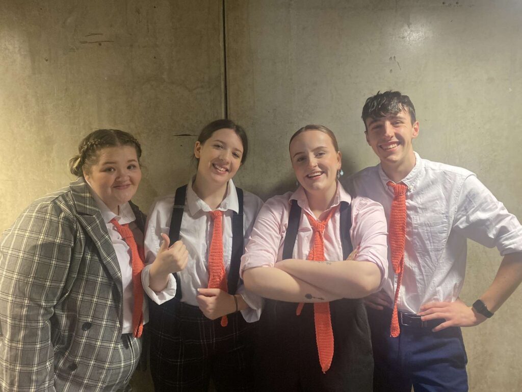 four students stand wearing office clothes and red ties