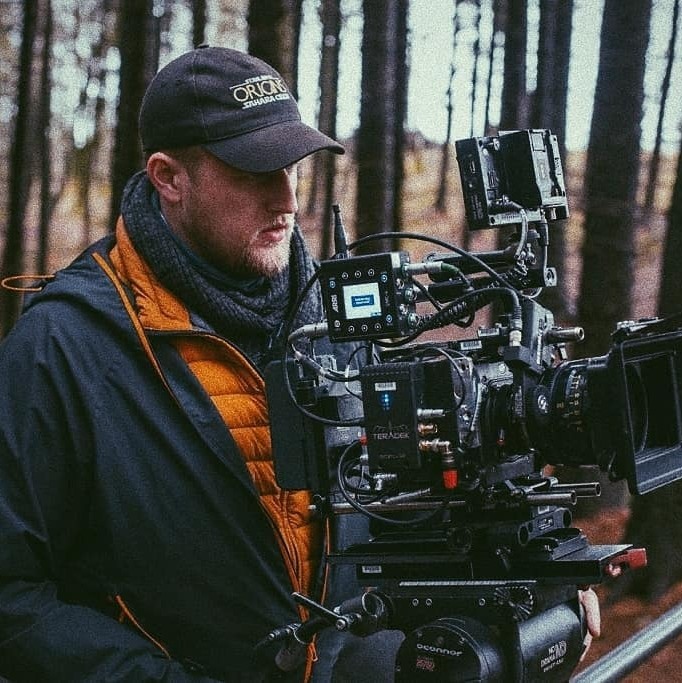 James Oldham on set with camera with trees in background