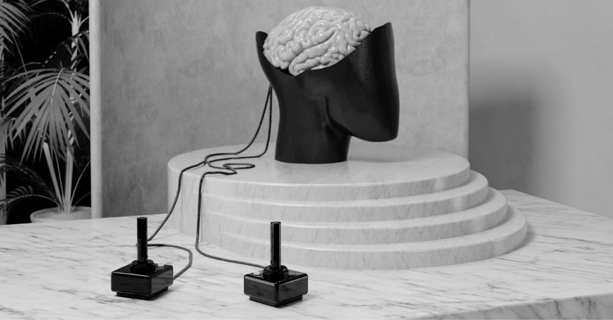 Sculpture of open head with brain inside attached to two gaming joysticks by wires