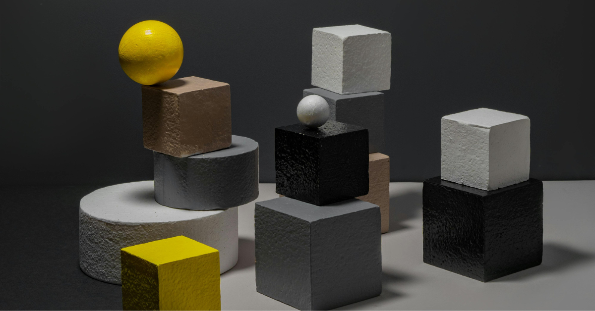 wooden shapes including cubes and spheres balancing on the edge of a table against a black background